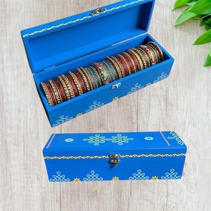 May include: A blue wooden bangle box with a hinged lid, decorated with yellow and white patterns. The box is open, revealing a collection of colorful bangles. The closed box is also visible, showcasing the same design.