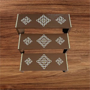 May include: A three-tiered, brown wooden shelf unit with decorative white and yellow geometric patterns. The edges are trimmed with a white and yellow zigzag design. The unit is displayed on a wooden surface.
