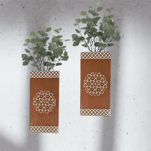 May include: Two brown wooden wall planters with white geometric designs and gold accents. Each planter has a leafy green plant inside.