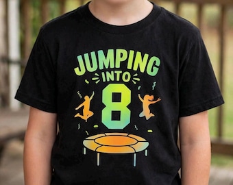 Könnte beinhalten: Ein schwarzes Kurzarm-T-Shirt mit einer bunten Grafik und dem Text JUMPING INTO 8. Das Design zeigt eine große Zahl 8, die Silhouetten von zwei springenden Personen und eine Trampolin-Illustration in den Farben Grün, Gelb und Orange.