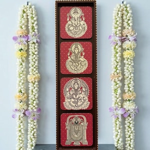 Pode incluir: Uma moldura vertical de madeira com quatro pain&eacute;is quadrados vermelhos, cada um com uma ilustra&ccedil;&atilde;o de uma divindade hindu em bege. Duas guirlandas de flores brancas, com detalhes em roxo e amarelo, ladeiam a moldura.