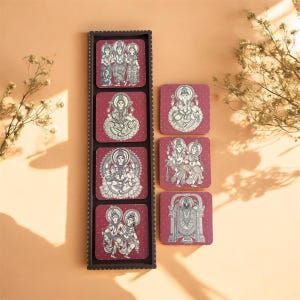 Pode incluir: Um conjunto de bases quadradas com figuras religiosas em branco sobre um fundo bord&ocirc;. As bases s&atilde;o exibidas em um suporte de madeira marrom escuro. As bases apresentam v&aacute;rias divindades e s&iacute;mbolos religiosos.