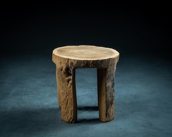 May include: A rustic wooden stool with a round top and three legs. The stool is made of natural wood with a rough, textured surface.