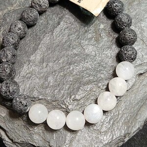 May include: A black lava rock and white moonstone beaded bracelet. The bracelet has a tag that says "Lava Love".
