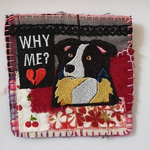 Peut inclure: Écusson brodé représentant un chien noir et blanc avec une expression triste. Le patch comprend le texte "WHY ME?" au-dessus d'un cœur brisé. Il est cousu sur un fond patchwork avec divers motifs et couleurs de tissu, dont des motifs rouges, blancs et floraux.