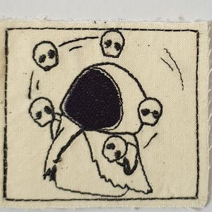 Puede incluir: Parche bordado con un diseño en blanco y negro de una figura rodeada de calaveras. La figura tiene una forma grande y oscura en la espalda y está rodeada de cinco calaveras. El parche es rectangular con un borde cosido negro.