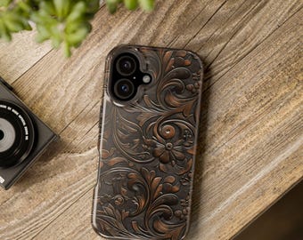 Peut inclure: Un étui de téléphone à motifs floraux marron et bronze. L'étui présente un motif en relief détaillé de fleurs et de feuilles tourbillonnantes. L'étui est sur une surface en bois, avec un appareil photo et une plante en arrière-plan.