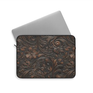May include: A laptop sleeve with an embossed floral design in brown and copper tones. The pattern includes flowers, leaves, and swirling details. A silver laptop is partially inserted, highlighting the sleeve's protective function.
