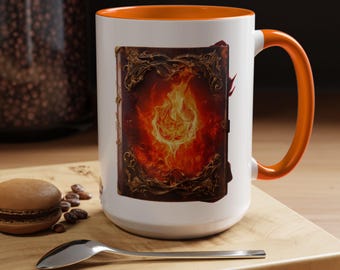 May include: A white ceramic mug with a bright orange interior and handle. The exterior features a graphic print of an ornate, dark-bound book with intricate gold-colored filigree corners and a vibrant, glowing fire centered on the front cover.