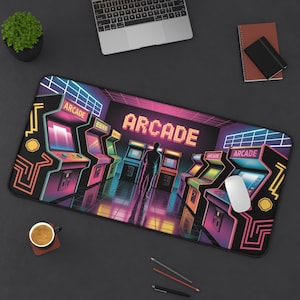 May include: A black desk mat featuring a retro arcade game design. The mat displays a neon-lit arcade scene with game machines and the word "ARCADE" in pixelated letters. A white mouse sits on the mat.
