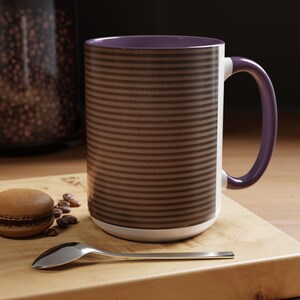May include: A coffee mug with a brown horizontal striped pattern, a purple interior, and a purple handle. The mug sits on a wooden surface with a macaron, coffee beans, and a spoon.