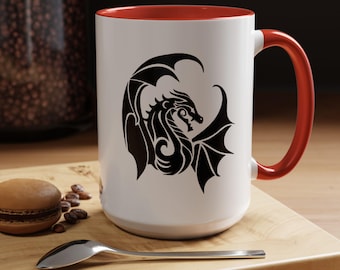 May include: A white ceramic mug with a bright red interior and a matching red handle. The exterior features a black tribal-style dragon graphic printed on the front. The mug has a cylindrical shape and a smooth finish, showcasing a bold contrast.
