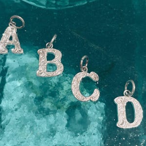 May include: Four silver charms in the shape of the letters A, B, C, and D. Each letter has an intricate, ornate design.