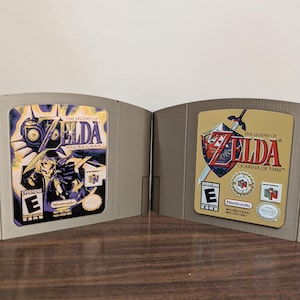 May include: Two Nintendo 64 game cartridges. One features the text "The Legend of Zelda: Majora's Mask" with a purple and black design. The other says "The Legend of Zelda: Ocarina of Time" with a gold and red design.