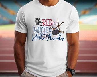 Op de afbeelding: Wit T-shirt met een rood-wit-blauw grafisch ontwerp. De afbeelding toont ijshockey schaatsen, een hockeystick, een puck en vuurwerk. De tekst luidt "Red White & Hot Tricks".