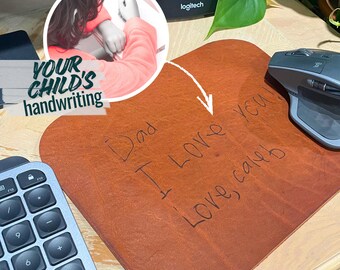 May include: A brown leather mousepad with a handwritten message that reads "Dad I Love you Love, Caleb." A gray wireless mouse sits on the pad. The words "YOUR CHILD'S handwriting" are in the upper left corner.