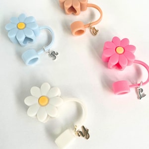 May include: Three silicone daisy flower bottle stoppers with a gold charm. The stoppers are in blue, pink, and white.
