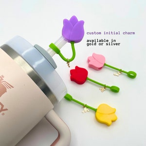 May include: Four colorful silicone tulip-shaped straw toppers with green stems and gold initial charms. The charms are available in gold or silver.  The toppers are shown on top of a pink and silver tumbler.