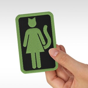 Op de afbeelding: Groen geborduurd patch met een zwarte omtrek. De patch toont een gestileerde vrouwelijke figuur met een kattenstaart.