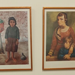 Puede incluir: Dos pinturas enmarcadas, ambas representando mujeres y niños. La pintura de la izquierda muestra a una niña con un suéter verde y una falda marrón de pie frente a una pared de ladrillo. La pintura de la derecha muestra a una mujer con un vestido rojo y una bufanda sosteniendo a un niño pequeño con un suéter azul.
