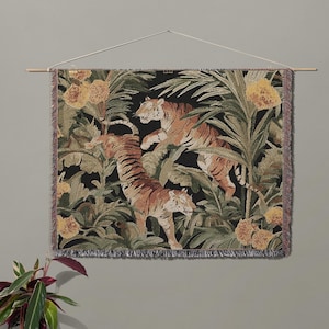 Puede incluir: Un tapiz de pared tejido rectangular que muestra dos tigres en un entorno de selva exuberante con hojas de palma verdes y flores amarillas sobre un fondo negro. El tejido tiene un borde con flecos y cuelga de una varilla de madera con un cord&oacute;n blanco.