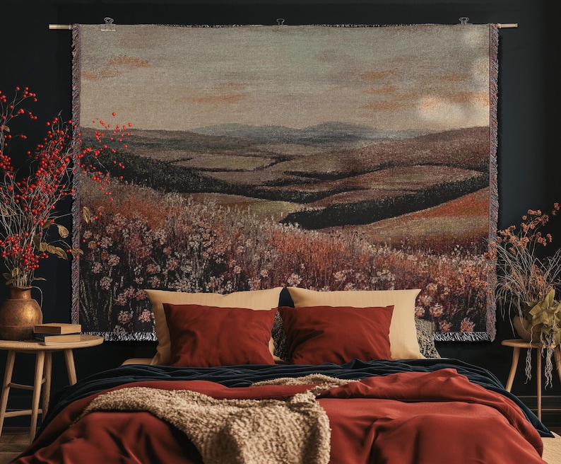 May include: A landscape tapestry featuring rolling hills and fields in brown, green, and beige tones. It hangs above a bed with red bedding and pillows. The room is decorated with wooden side tables and vases, creating a warm atmosphere.