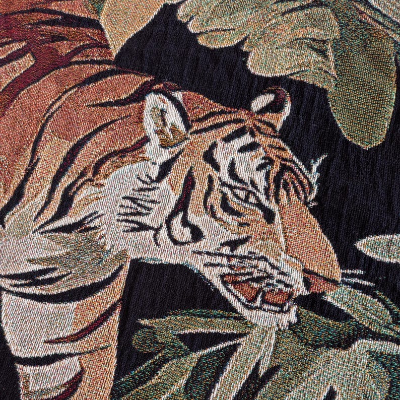 Puede incluir: Un tejido textil con un patr&oacute;n detallado de tigre en tonos naranja, negro y blanco. El tigre aparece representado entre grandes hojas verdes texturizadas sobre un fondo negro s&oacute;lido, mostrando un complejo tejido de hilos multicolor.