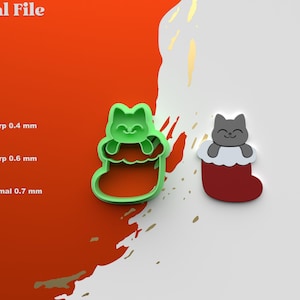 以下が含まれることがあります： サンタの帽子をかぶった猫が描かれたクリスマスストッキングのクッキーカッターの3DプリントSTLファイルです。カッターは緑色で、猫は灰色です。画像には、赤と白のストッキングに灰色の猫が描かれています。