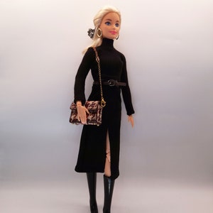 May include: A blonde doll wearing a black turtleneck dress with a black belt and a brown and black patterned handbag. The doll is wearing black boots and has gold hoop earrings.