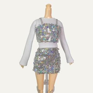 May include: A white long-sleeved top with a silver sequined crop top and matching skirt. The skirt is a mini skirt with a high waist.