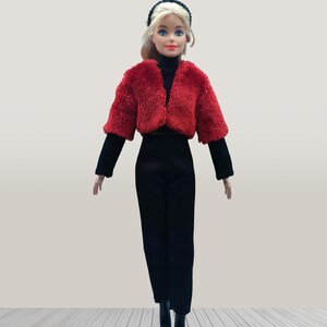 May include: A doll wearing a red faux fur cropped jacket, black turtleneck, and black pants. The doll has blonde hair and is wearing a black headband and black boots. The doll is standing on a light wood floor.