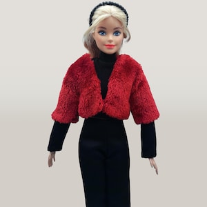 May include: A doll wearing a red fuzzy cropped jacket, black turtleneck, black pants, and a black headband. The doll has blonde hair and blue eyes. The outfit is a fashion statement.