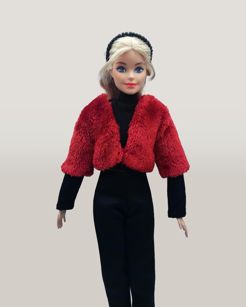 May include: A doll wearing a red fuzzy cropped jacket, black turtleneck, black pants, and a black headband. The doll has blonde hair and blue eyes. The outfit is a fashion statement.