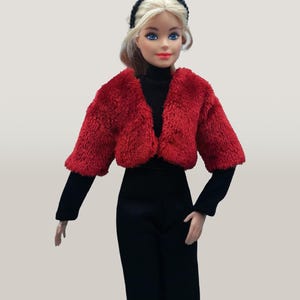 May include: A doll wearing a red faux fur jacket, black turtleneck, and black pants. The doll has blonde hair, blue eyes, and a black headband. The outfit is a fashion statement.