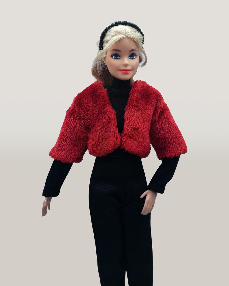 May include: A doll wearing a red faux fur jacket, black turtleneck, and black pants. The doll has blonde hair, blue eyes, and a black headband. The outfit is a fashion statement.