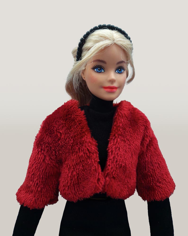 May include: A doll with blonde hair, blue eyes, and red lipstick, wearing a black turtleneck and a short, fluffy red jacket. A black beaded headband adorns the doll's hair. The doll is dressed in a fashion-forward style.