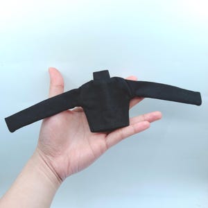 May include: A small, black long-sleeved shirt with a mock neck. The shirt is displayed with the sleeves extended. The garment is made of a soft, dark fabric.