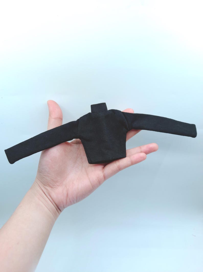 May include: A small, black long-sleeved shirt with a mock neck. The shirt is displayed with the sleeves extended. The garment is made of a soft, dark fabric.