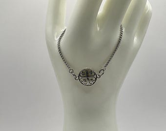 Könnte beinhalten: Ein silbernes Armband mit einem runden Anhänger, der ein Kleeblatt-Design zeigt.