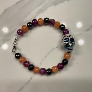 Halloween beaded bracelet with cute skull. Purple, orange, and black beads. Boho handmade Halloween bracelet. Beaded skull bracelet.