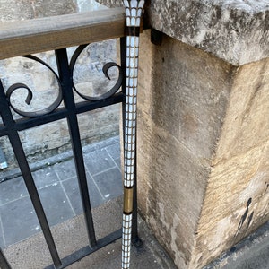 Puede incluir: Un bast&oacute;n blanco y dorado con una parte superior decorativa. El bast&oacute;n est&aacute; hecho de madera y tiene un patr&oacute;n blanco y dorado.