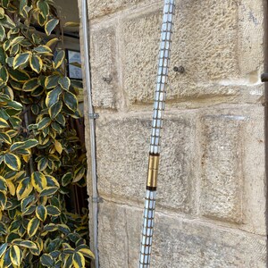 Puede incluir: Un bast&oacute;n blanco y dorado con una parte superior decorativa. El bast&oacute;n est&aacute; hecho de n&aacute;car y tiene una banda de lat&oacute;n alrededor del medio.