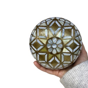 Könnte beinhalten: Eine weiße und goldene Dekorkugel mit einem geometrischen Muster aus Perlmutt und Messing.