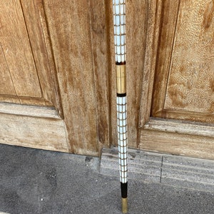 Puede incluir: Un bast&oacute;n con un dise&ntilde;o de mosaico blanco y dorado. El bast&oacute;n tiene un mango negro y una punta dorada.