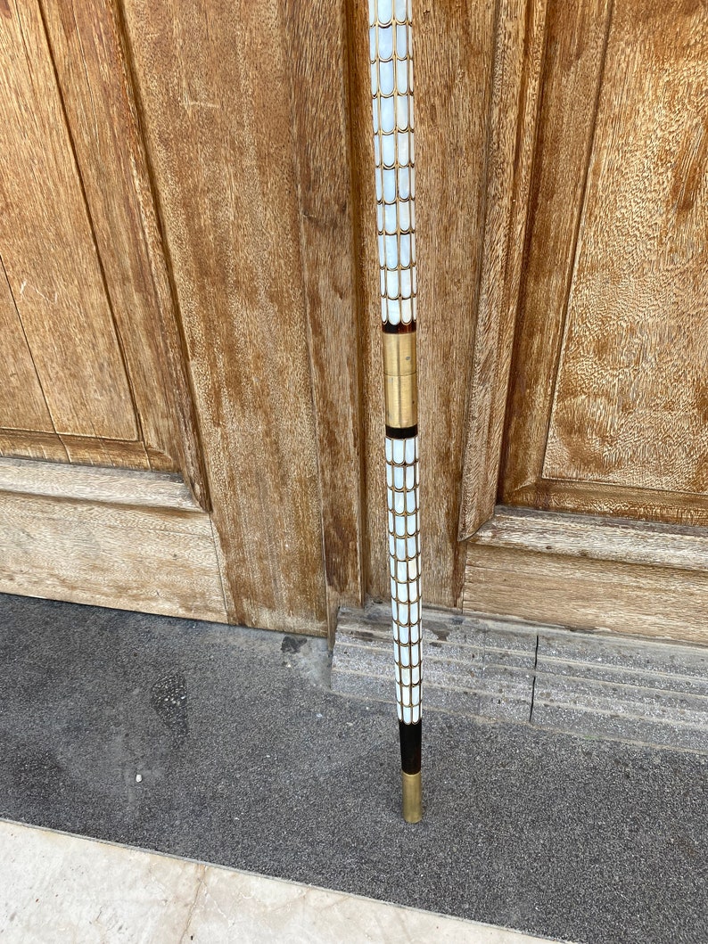 Puede incluir: Un bast&oacute;n con un dise&ntilde;o de mosaico blanco y dorado. El bast&oacute;n tiene un mango negro y una punta dorada.