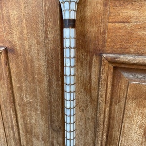 Puede incluir: Un bast&oacute;n blanco y dorado con una parte superior decorativa hecha de n&aacute;car.