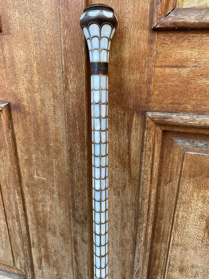 Puede incluir: Un bast&oacute;n blanco y dorado con una parte superior decorativa hecha de n&aacute;car.