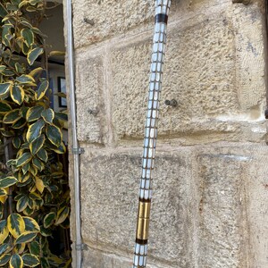 Puede incluir: Un bast&oacute;n de paseo con un eje de patr&oacute;n blanco y dorado y una parte superior de color marr&oacute;n oscuro. El bast&oacute;n est&aacute; hecho de madera y tiene un dise&ntilde;o decorativo.