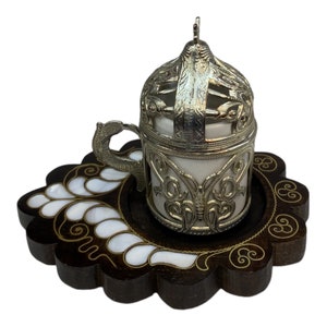 May include: A silver and white Turkish coffee cup and saucer set with intricate filigree designs. The saucer is made of wood with mother-of-pearl inlay.