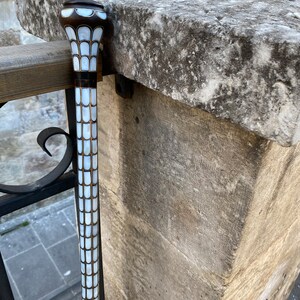 Puede incluir: Un bast&oacute;n blanco y marr&oacute;n con una parte superior decorativa hecha de azulejos de n&aacute;car blanco.